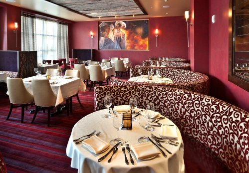Elegant restaurant interior with round tables, plush seating, and warm lighting, featuring a large artwork on the wall.