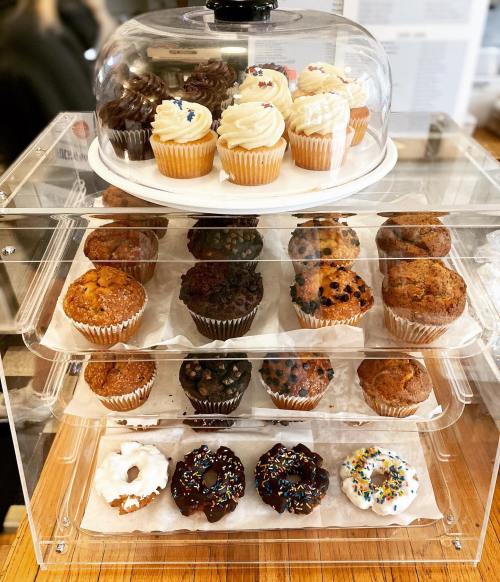 A display of assorted cupcakes and muffins under a glass dome, featuring various flavors and toppings.