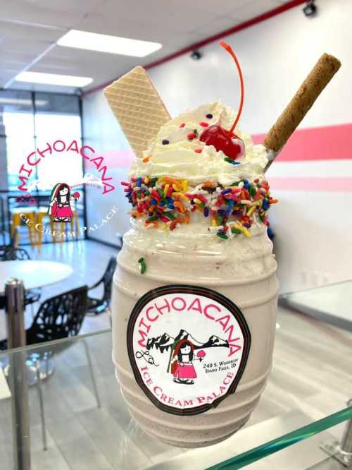 A colorful milkshake topped with whipped cream, a cherry, sprinkles, and wafer sticks in a jar at an ice cream shop.