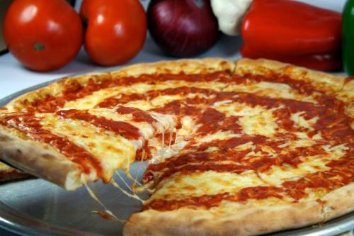A freshly baked cheese pizza with a slice being pulled away, surrounded by fresh vegetables.