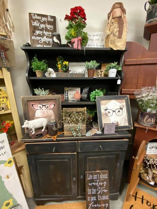 A rustic display featuring a black cabinet, decorative plants, framed art, and a sign with a motivational quote.