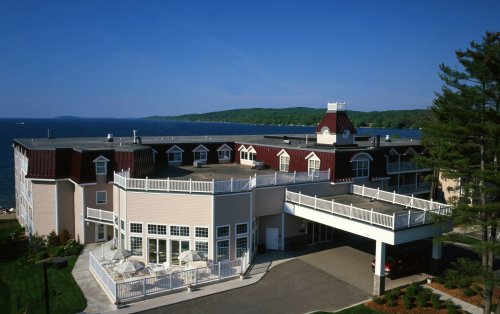 A waterfront hotel with a large deck, surrounded by trees and a scenic view of the water in the background.