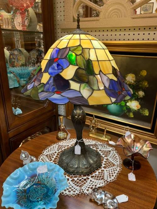 A stained glass lamp with a floral design sits on a table, surrounded by decorative items and a lace doily.