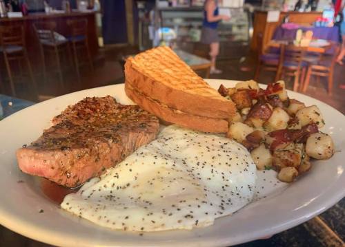 A plate of steak, two fried eggs, toast, and seasoned potatoes served in a restaurant setting.