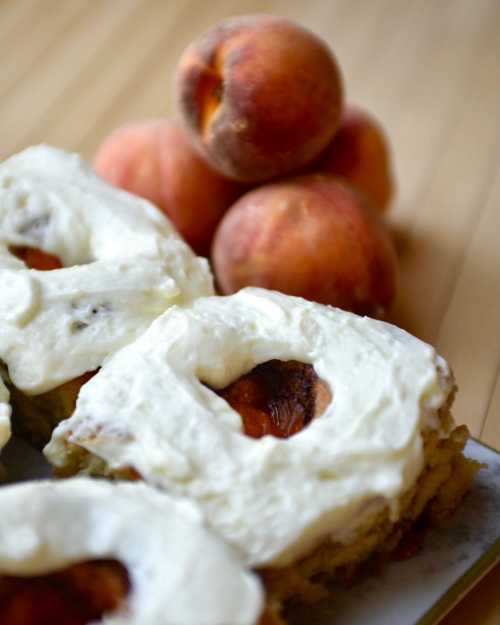 Peach dessert with cream frosting, featuring sliced peaches in the foreground and whole peaches in the background.