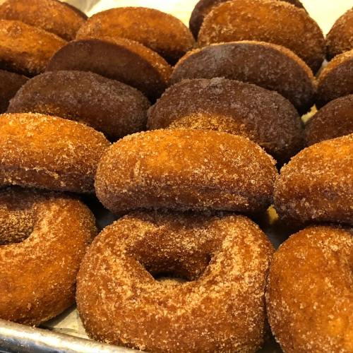 A close-up of freshly made, golden-brown donuts coated in sugar, arranged on a tray.
