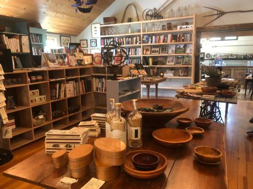 A cozy shop interior featuring wooden tables, shelves of books, and various handcrafted items on display.