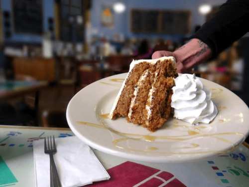 A slice of layered cake with whipped cream on a plate, being served in a cozy café setting.