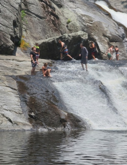 People enjoying a sunny day by a waterfall, playing in the water and relaxing on the rocks.