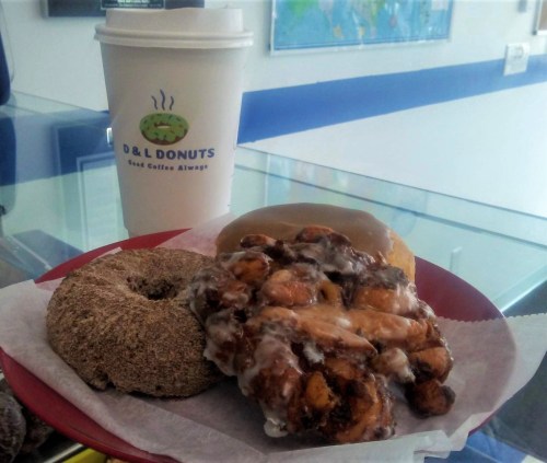 A plate with three donuts: a glazed donut, a cinnamon sugar donut, and a cinnamon roll, alongside a coffee cup.