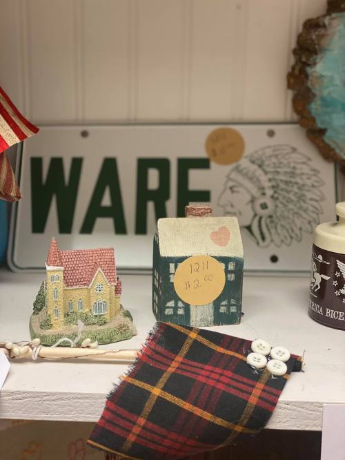 A display of decorative items including small houses, a plaid fabric, and a vintage license plate in the background.