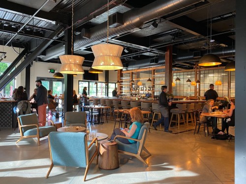 A modern restaurant interior with patrons seated at tables and a bar, featuring stylish lighting and comfortable seating.