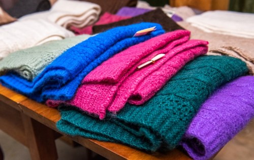 A colorful assortment of folded knitted scarves in various shades, displayed on a wooden table.