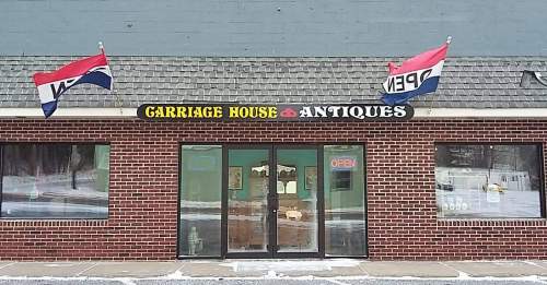 Front view of "Carriage House Antiques" store with flags and a snow-covered sidewalk.