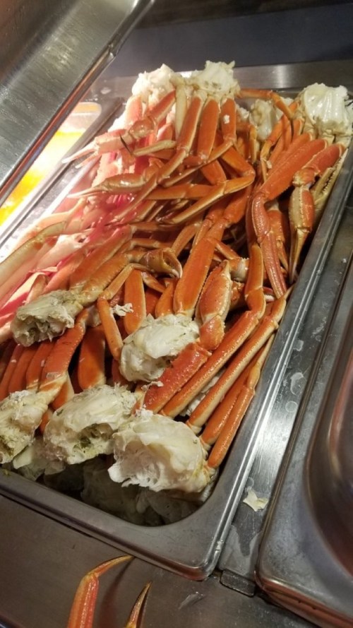 A metal tray filled with a large quantity of cooked crab legs and claws, showcasing their orange and white colors.