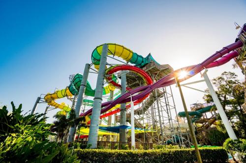 Colorful water slides twist and turn against a clear blue sky, surrounded by lush greenery.