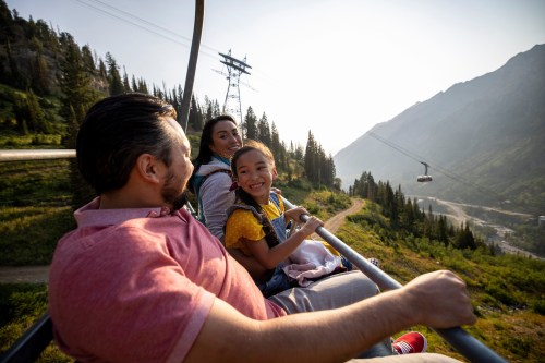 A family enjoys a scenic chairlift ride through a mountainous landscape, smiling and taking in the view.