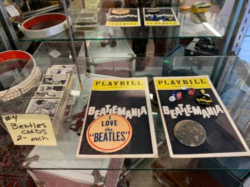 Display case with Beatles memorabilia, including Playbills for "Beatlemania" and a sign for Beatles cards priced at $4 each.
