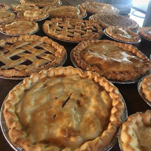 A variety of freshly baked pies arranged on a wooden table, showcasing different crust designs and fillings.