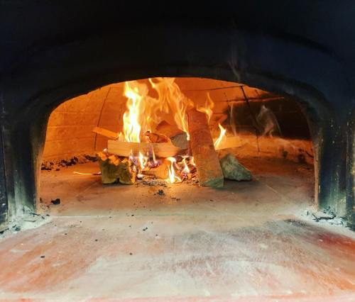 A warm, glowing fire burns inside a brick oven, with flames and wood visible in the hearth.