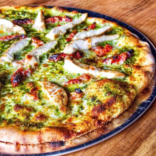 A freshly baked pizza topped with pesto, grilled chicken, and cherry tomatoes on a golden crust.