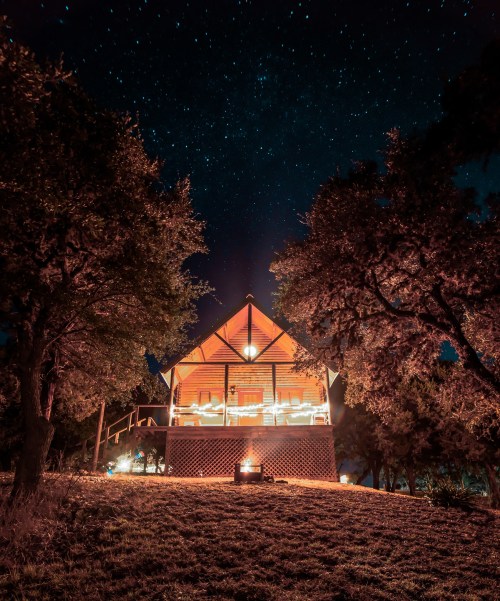 A cozy cabin illuminated at night, surrounded by trees under a starry sky.