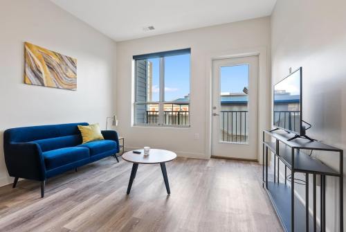 Bright living room with a blue sofa, coffee table, and TV, featuring large windows and modern decor.