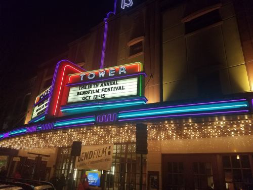 Neon-lit Tower Theatre marquee announcing the BendFilm Festival, October 12-15, with festive lights.