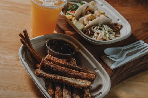 A tray with tacos, a side of beans, and cinnamon sticks, alongside a drink in a cup.
