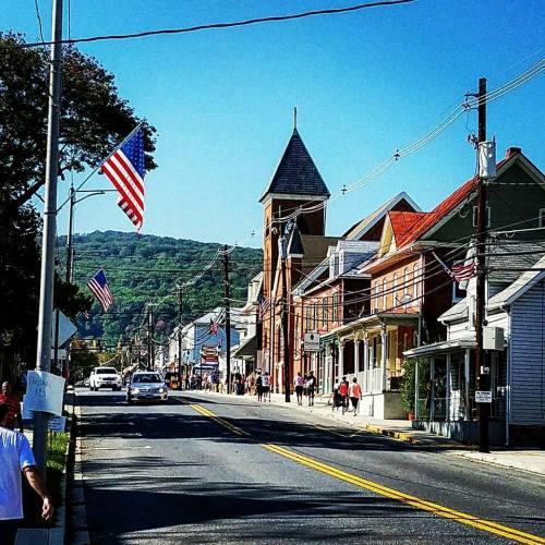 A street view featuring buildings, an American flag, and a mountain in the background on a sunny day.