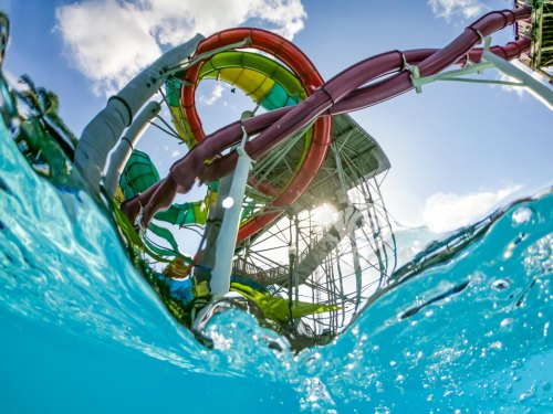 Colorful water slides tower above a clear blue pool, with sunlight sparkling on the water's surface.