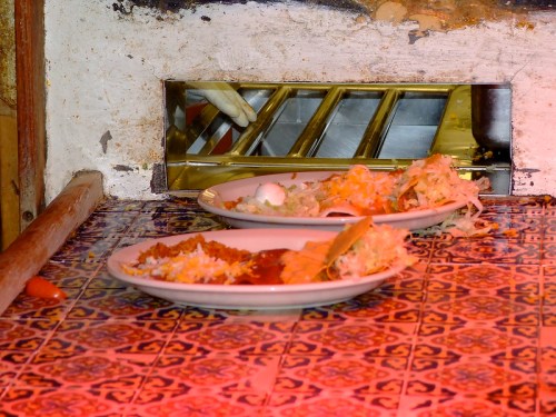 Two plates of food on a tiled surface, with a small opening in the wall behind them.