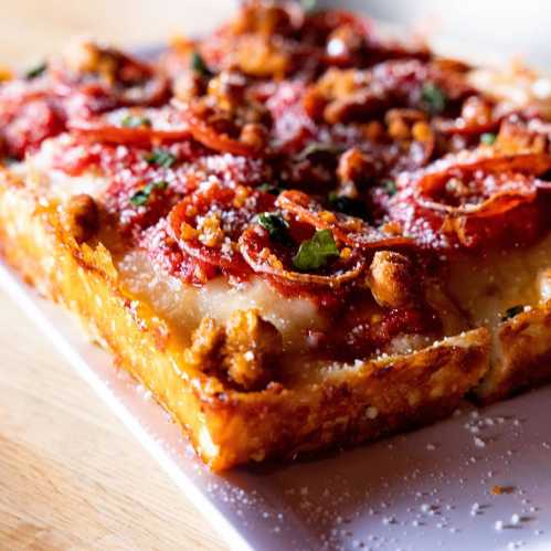 A close-up of a cheesy pizza topped with crispy pepperoni and herbs on a wooden surface.