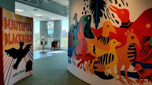 Colorful mural of birds on a wall, with a sign reading "Beautiful Blackbird" in a bright, inviting space.