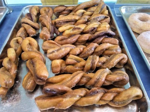 A tray of twisted, golden-brown pastries with a shiny glaze, arranged neatly alongside some donuts.