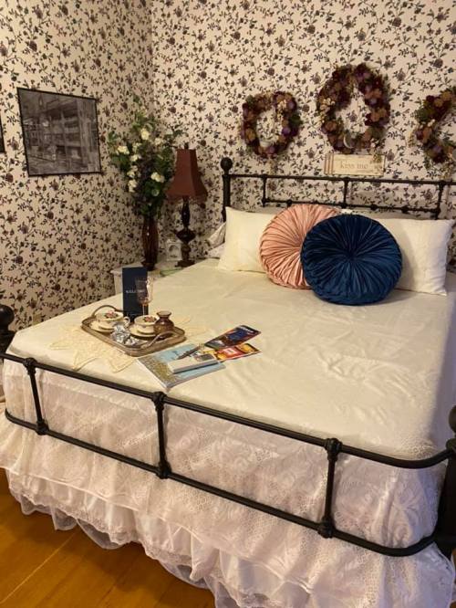 A cozy bedroom with a floral wallpaper, a bed adorned with pillows, and a tray of tea on a white bedspread.