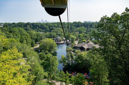 Aerial view of a lush green landscape with a lake and buildings, framed by trees and a clear blue sky.
