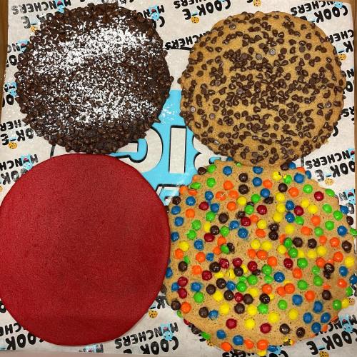 A variety of large cookies: one with chocolate chips, one with colorful candies, and a red circular cookie.