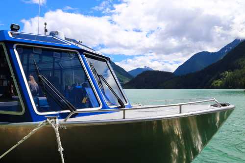 A close-up of a boat on calm water, surrounded by mountains and a partly cloudy sky.