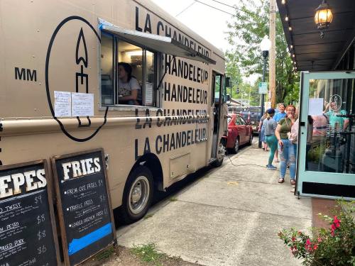A food truck named "La Chandeleur" parked on a street, with a line of customers waiting outside.