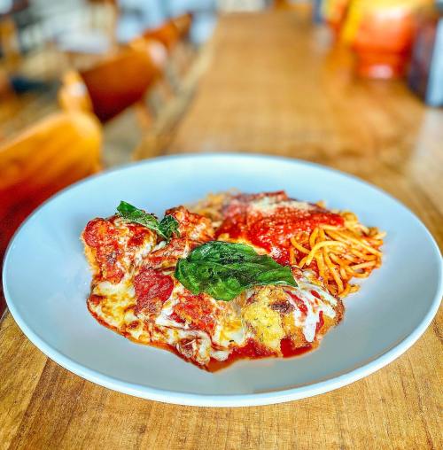 A plate of baked pasta with marinara sauce, melted cheese, and fresh basil, served on a wooden table.