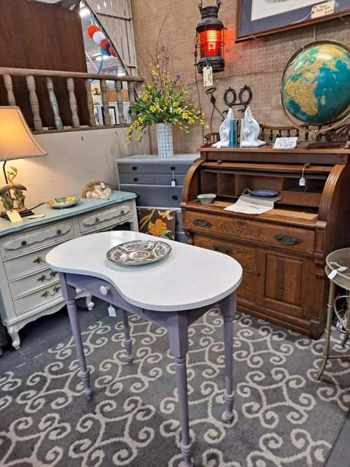 A cozy vintage display featuring a purple table, antique furniture, a globe, and decorative items in a charming setting.