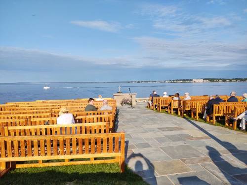 Outdoor seating arranged for an event by the water, with a clear sky and distant shoreline visible.