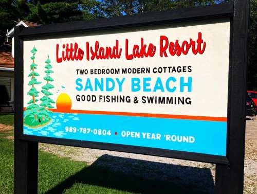 Sign for Little Island Lake Resort featuring cottages, sandy beach, and activities like fishing and swimming. Open year-round.