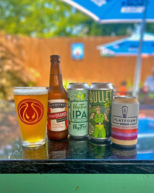 A glass of beer next to three cans of craft beer on a table, with a blurred outdoor background.