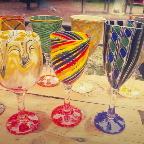 A collection of colorful, hand-blown glass goblets with various swirling patterns displayed on a wooden table.