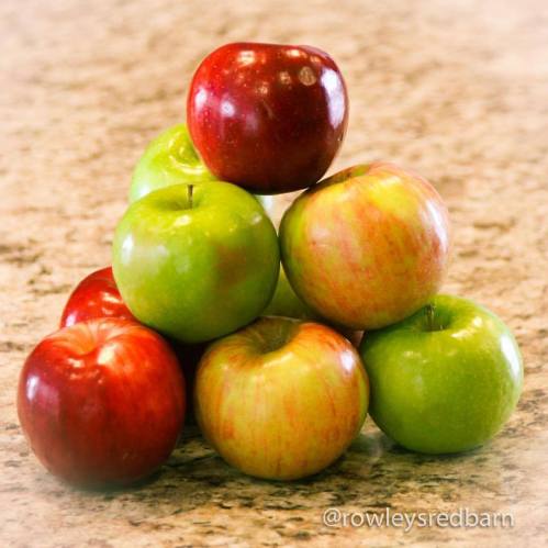 A pyramid of red and green apples stacked on a countertop.