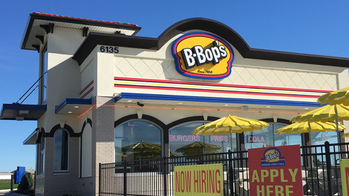 Exterior of B'Bop's restaurant with a bright sign, yellow umbrellas, and a "Now Hiring" banner.