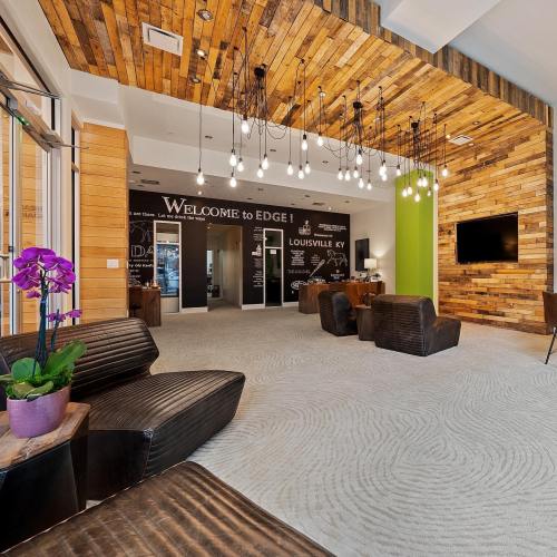 Modern lobby with wooden walls, stylish seating, and pendant lights, featuring a welcome sign and a TV.