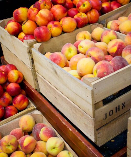 Baskets of fresh peaches in wooden crates at a market, showcasing a variety of colors and ripeness.